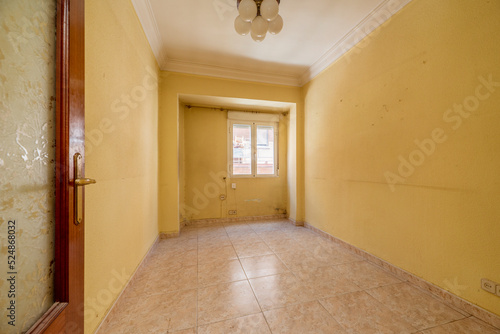 Empty room with light stoneware floor, dirty yellow painted walls, aluminum window with view and plaster trim on ceilings