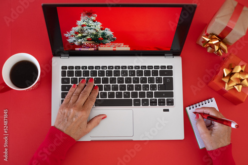 Woman's hands browsing on laptop at Christmas time - red background with Christmas presents