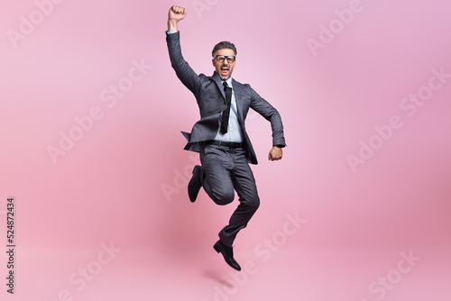 Excited mature man in full suit jumping and gesturing against pink background