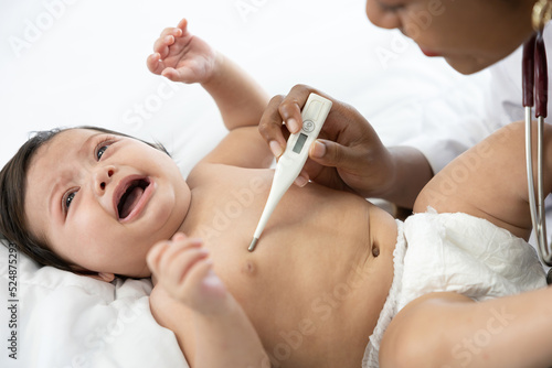 doctor measuring baby's temperature and baby crying on bedroom © offsuperphoto