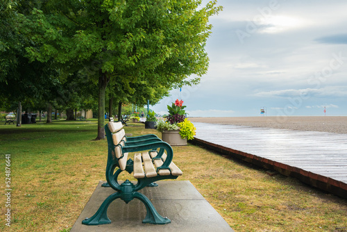 A park bench with green arms on a wooden boardwalk and an empty beach after a rain storm in Toronto's Beaches neighbourhood shot in August.	 photo