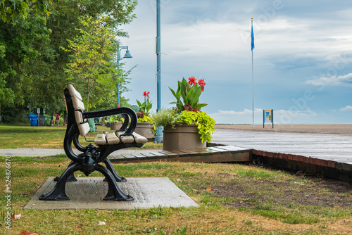 A park bench with black arms on a wooden boardwalk and an empty beach after a rain storm in Toronto's Beaches neighbourhood shot in August.	 photo