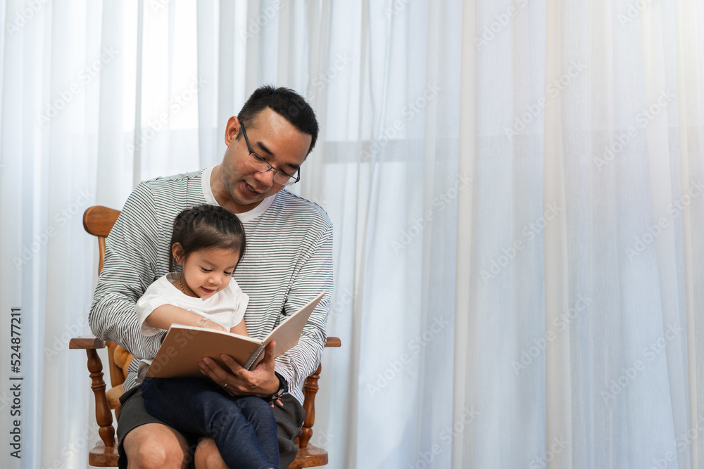 Asian father reading storybook to daughter in living room, family concept and early childhood development Asian father reading storybook to daughter in living room, family concept and early childhood development