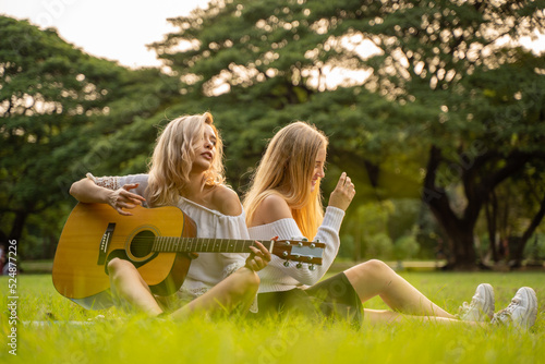 Portrait of caucasian young women sitting in the park outdoor and playing a guitar sing a song together with happiness