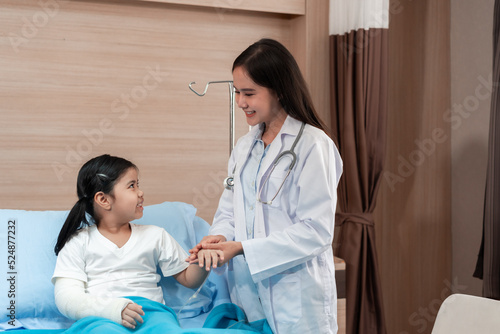 Pediatrician doctor examining little asian girl with a broken arm wearing a cast at hospital © ronnachaipark