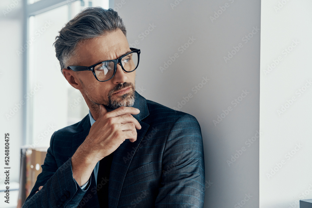 Thoughtful mature man in formalwear holding hand on chin while looking through a window Thoughtful mature man in formalwear holding hand on chin while looking through a window