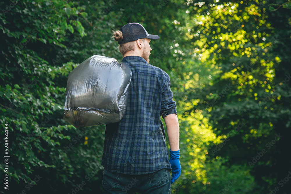 A young man in gloves and with a garbage bag cleans up in the forest. A young man in gloves and with a garbage bag cleans up in the forest.