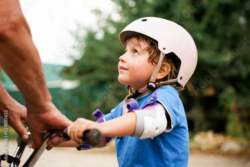 Grandfather teaching little child riding a bike. Toddler boy wearing safety helmet  learns cycling.