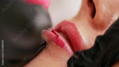 Permanent makeup procedure applying rose red pigment using tattoo machine in beautician salon. Microblading tattoo lips, close up 