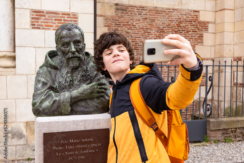 Teenager boy taking a selfie with a monument, making funny content for social media. Travelling student, sightseeing.