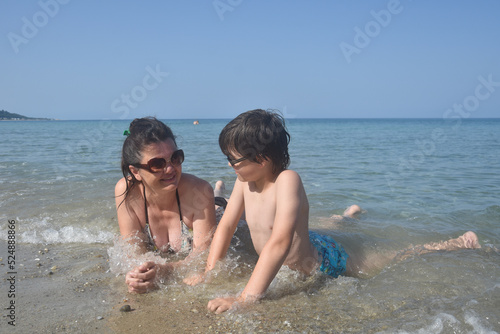 Happy family enjoy at beach. Summer vacation, smiling and joy in water. Mom with the small son on beach in the sea waves © Ivan