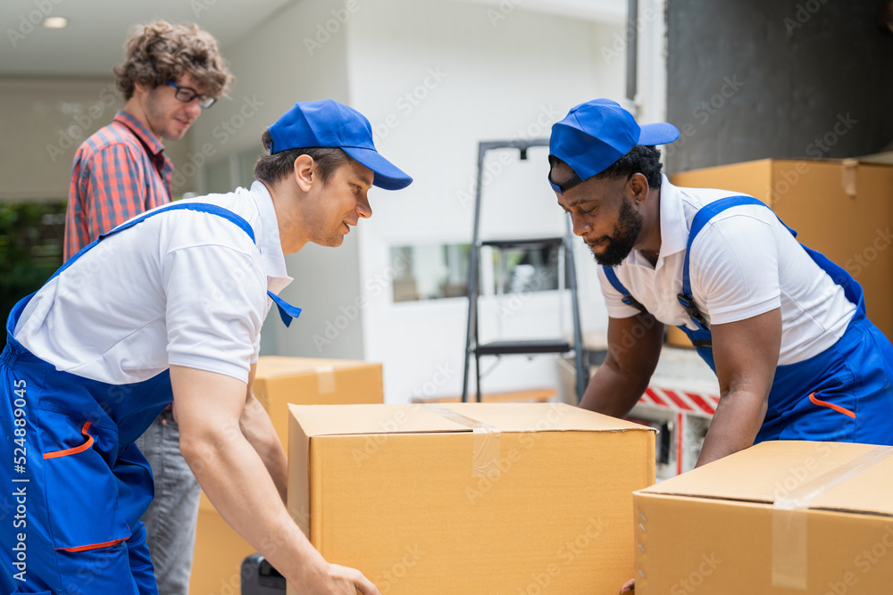 Man movers worker in blue uniform unloading cardboard boxes from truck.Professional delivery and moving service. Man movers worker in blue uniform unloading cardboard boxes from truck.Professional delivery and moving service.