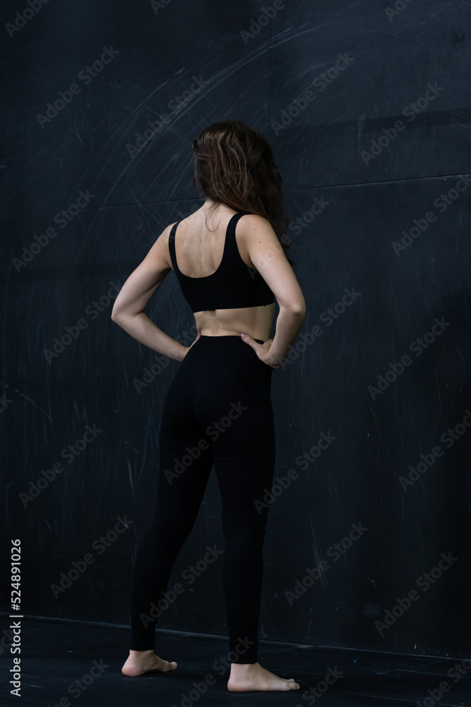 Young woman meditates, doing yoga poses and asana. Fitness girl enjoying yoga indoors. A yoga gymnast girl on a dark background. Black on Black. Young woman meditates, doing yoga poses and asana. Fitness girl enjoying yoga indoors. A yoga gymnast girl on a dark background. Black on Black.