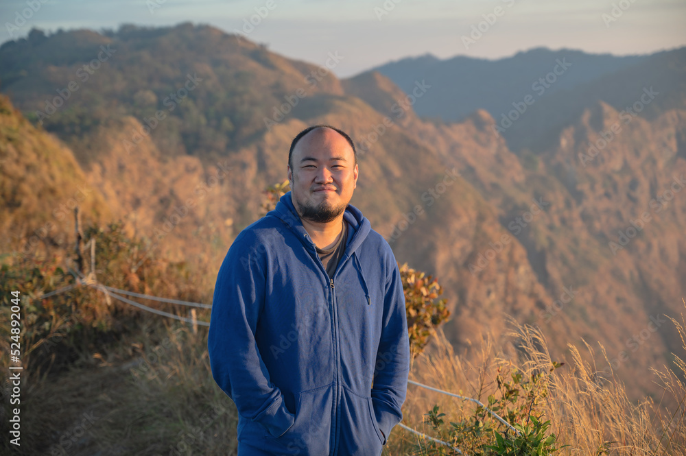 Asian fat man with beautiful sunrise of khao San nok wua mountain kanchanaburi.Khao San Nok Wua is the highest mountain in Khao Laem National Park. It is 1767 meters above sea level.