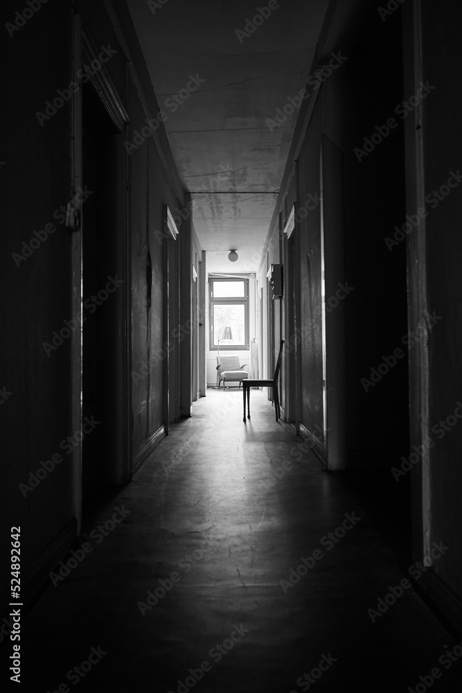 Bright sunlight shines through distant window in a dark and spooky hallway.