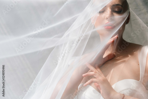 Bald beautiful bride in a luxurious wedding dress in red lipstick and a long veil is sick with cancer