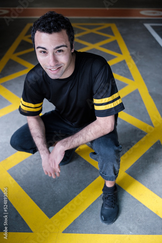 Young man is posing in a squat position looking at camera on a striped paint floor.
