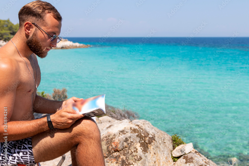 Handsome young man is lreading a book next to the see.Summer vacation concept. Handsome young man is lreading a book next to the see.Summer vacation concept.