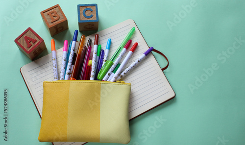 Bolsa amarilla con bolígrafos y plumones de colores sobre cuaderno abierto.  