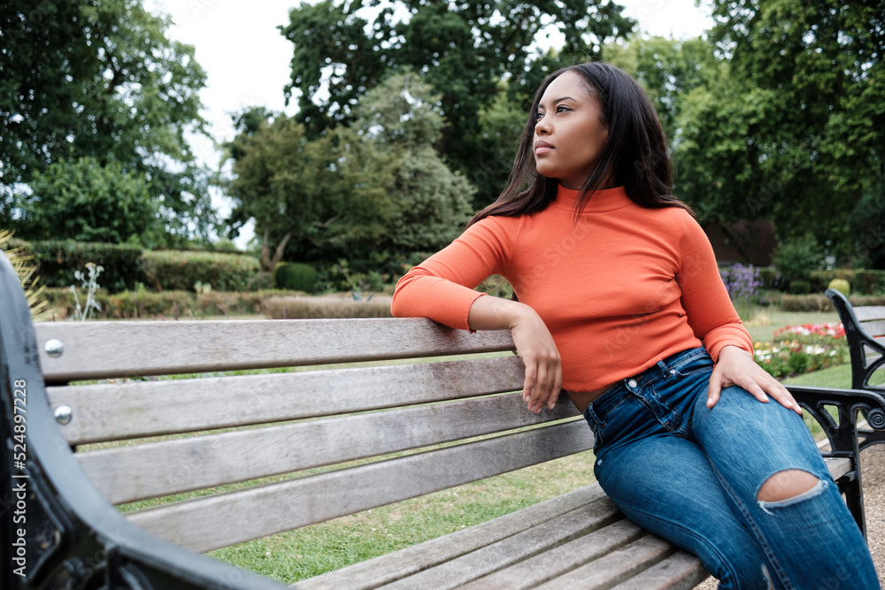 Portrait of serious young mixed race woman sitting on a bench on a park and looking away. Portrait of serious young mixed race woman sitting on a bench on a park and looking away.