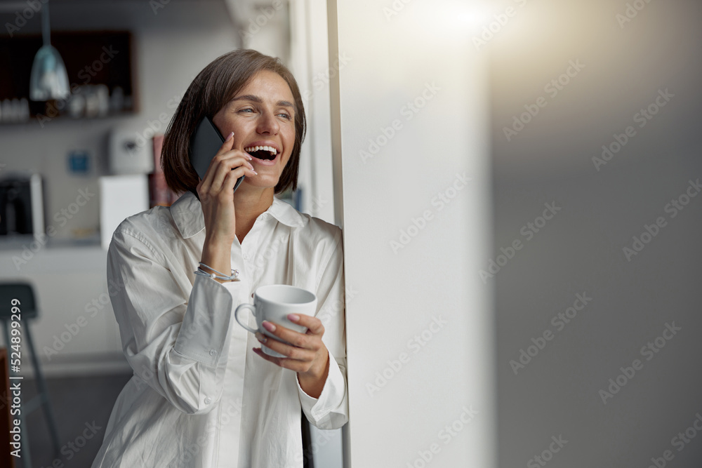 European business woman holding cup of coffee and talking phone while standing near window at office European business woman holding cup of coffee and talking phone while standing near window at office