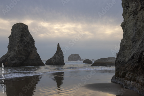 Sunset at the oregon coast on a dramatic cloudy day with reflections of the rocks in the sand