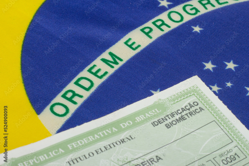 Obraz premium LAURO DE FREITAS, BRAZIL - August 19, 2022 : hand holding brazilian election document near brazilian flag