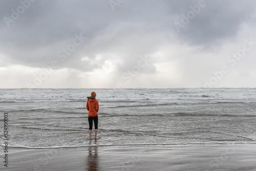 Картината върху платно Girl walks in orange coat and hat along the oregon coast during a cold rainy day