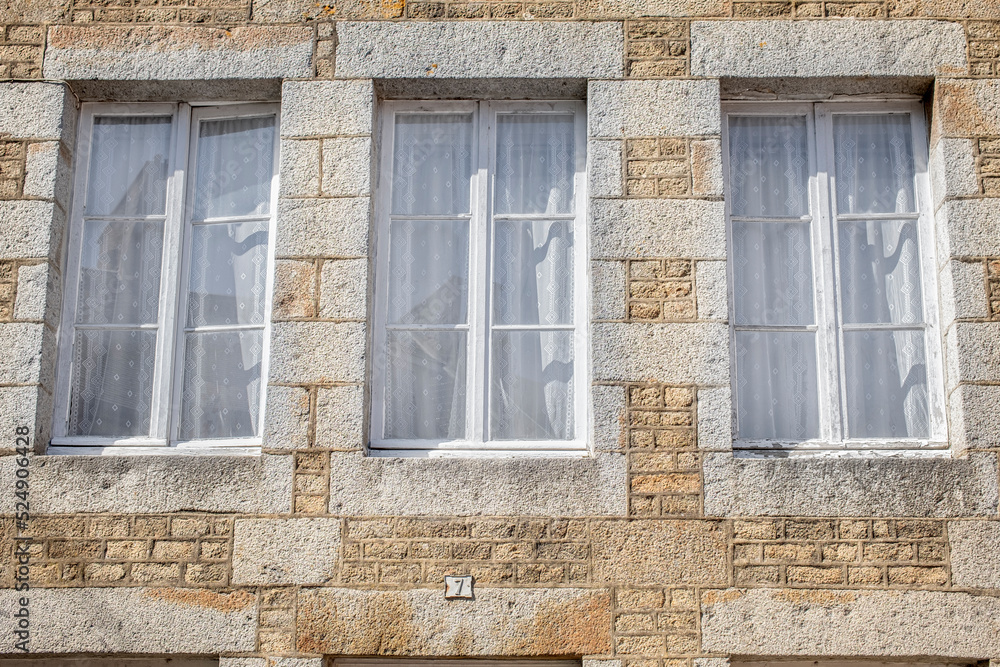 Detail of an old French Normandy house with three windows and closed curtains