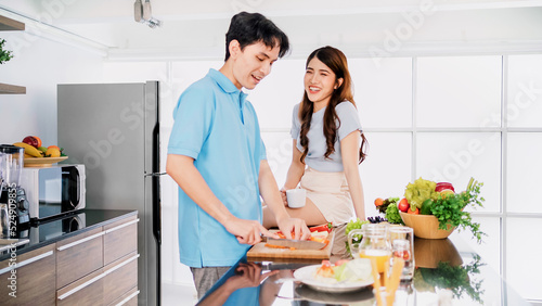 Asian cheerful loving couple talking, preparing and cooking with joy while standing on a kitchen counter at home. Cooking together in their home kitchens.