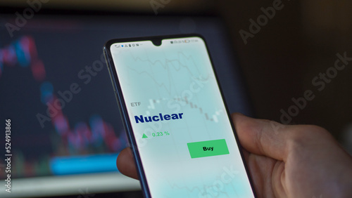 An investor's analyzing the nuclear energy etf fund on screen. A phone shows the nuclear ETF's prices nuclear energies to invest in power plants. 