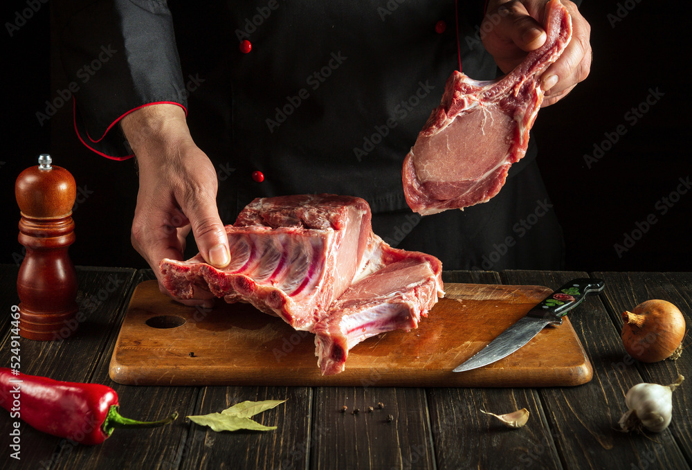 Butcher or chef is holding a piece of raw meat with a bone in the kitchen. Slicing pork ribs by the hands of a butcher