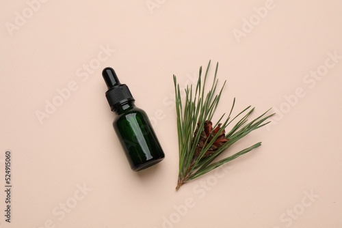 Glass bottle of essential oil and pine branch with cone on pink background, flat lay