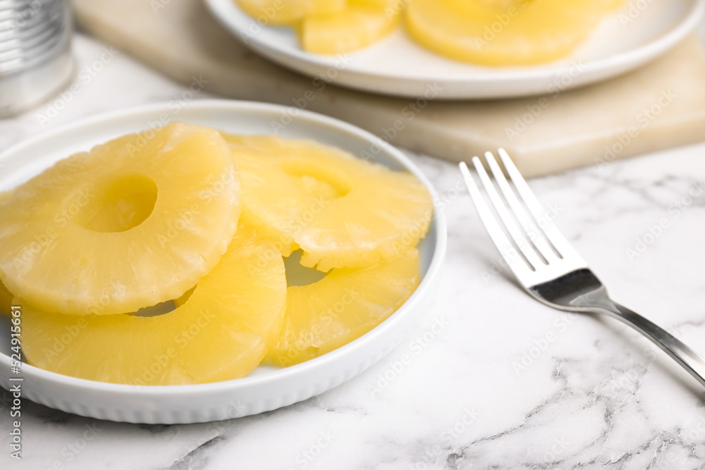 Tasty canned pineapple slices and fork on white marble table Tasty canned pineapple slices and fork on white marble table