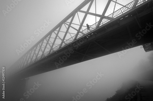 Woman walking alone across the bridge through dark winter mist