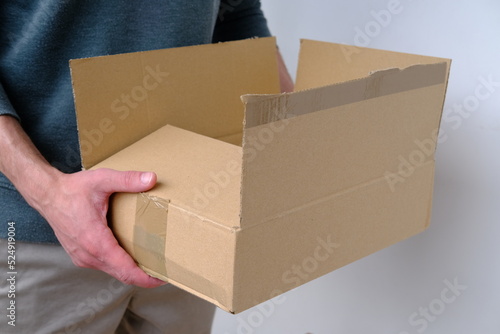 close-up of male hands open cardboard box of medium size stands on wooden stool, postal box with wrapping paper, a parcel, delivery of ordered goods, online shopping, timely delivery to customers © kittyfly