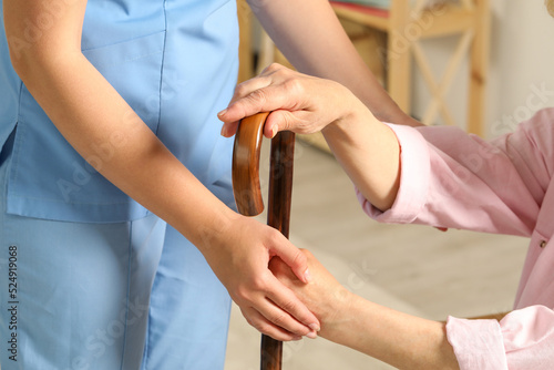 Elderly woman with walking cane and female caregiver indoors, closeup