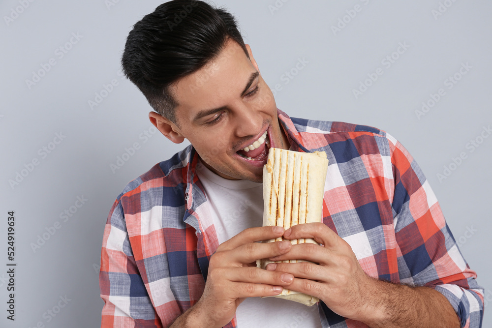 Man eating delicious shawarma on grey background