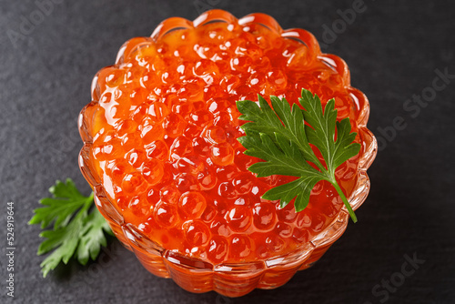 Salmon red caviar in a glass bowl on a black background. Crystal dish full of trout caviar close-up. Seafood fish delicacy of salted salmon roe. Texture of caviar. Gourmet food concept.