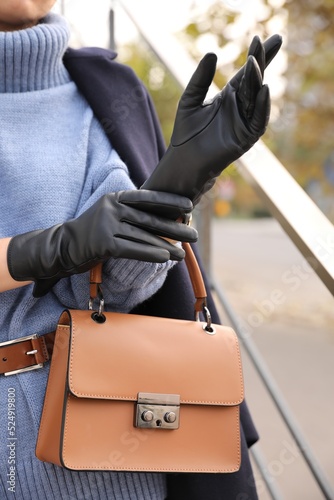 Young woman with stylish black leather gloves and bag outdoors, closeup