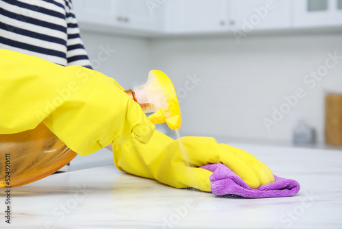 Woman cleaning white surface with detergent and purple rag indoors, closeup