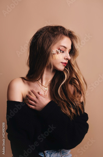 Portrait of a gentle girl with white flowers glued with a plaster to her cheek on a brown background in the studio.