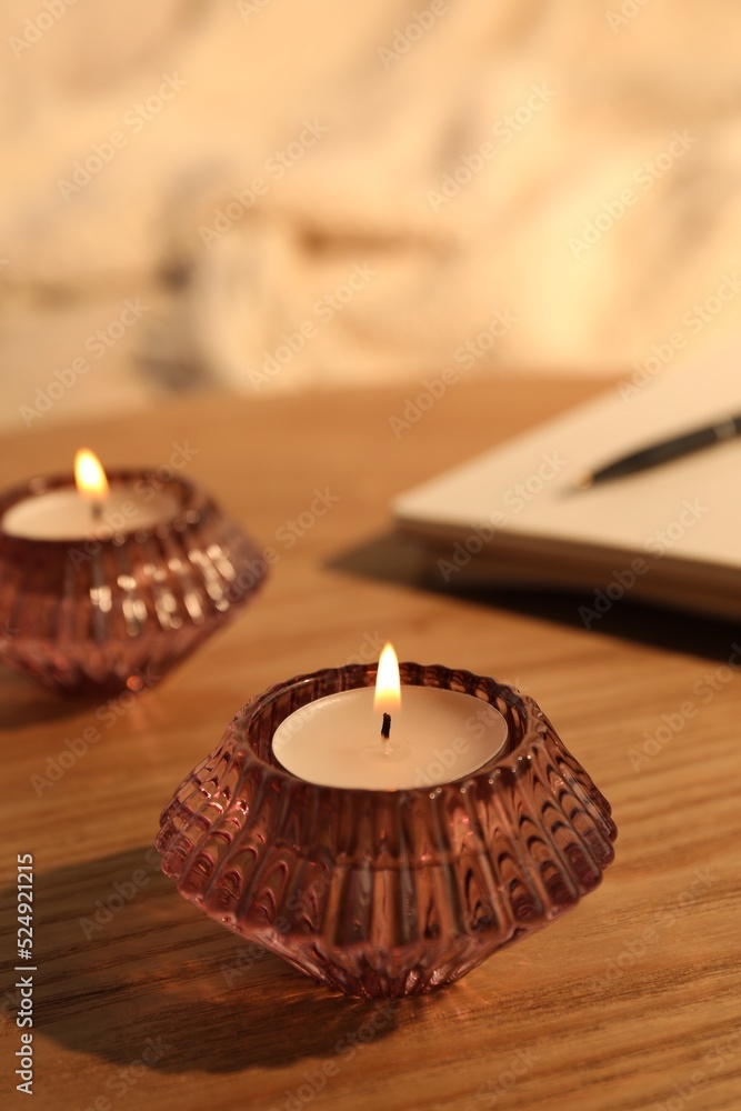 Burning candles in beautiful glass holders on wooden table indoors