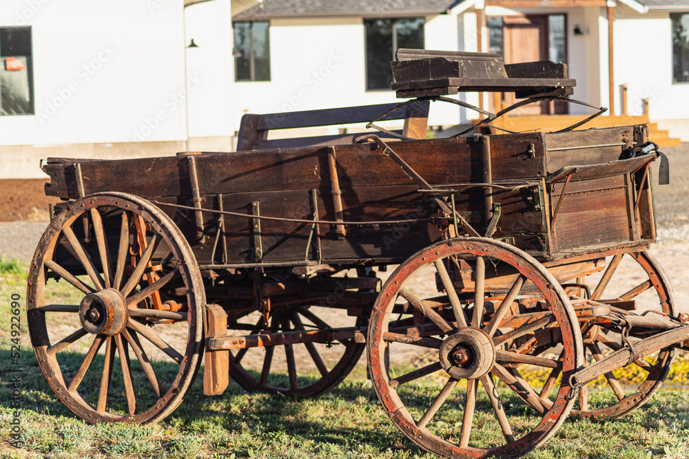 This is a digitally enhanced, color image of a buck board wagon.  The evening sunlight accentuates the textures as well as the orange and brown colors.  Out-of-focus home is in the background