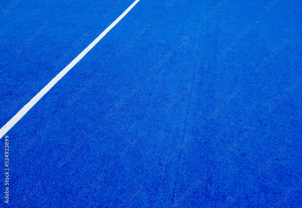 View of the net and the centre line of a blue paddle tennis court.