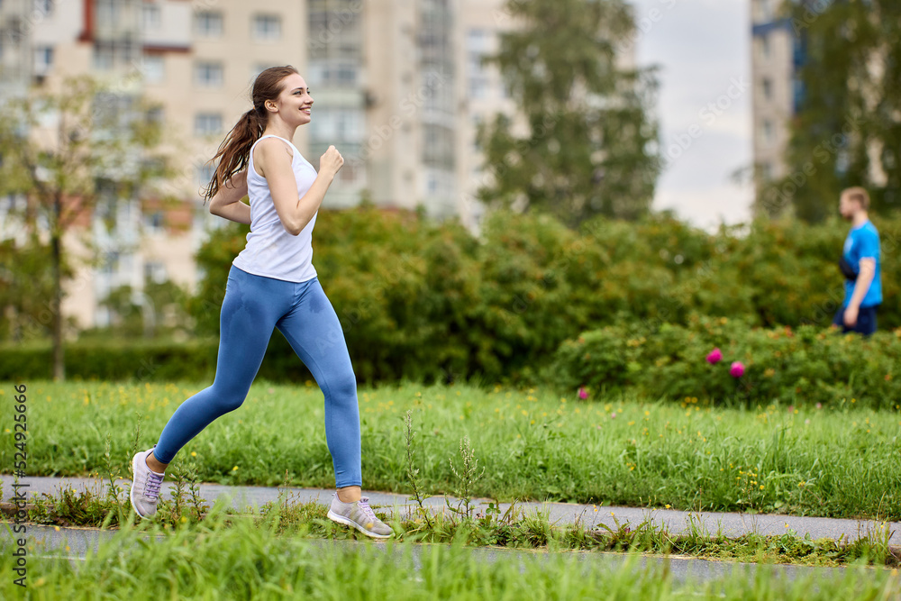 Smiling female runner trains in park area of residential area on summer morning.