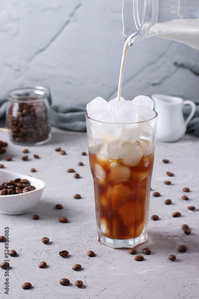 Cold coffee in a tall glass with cream being poured into it showing the texture of the drink. Light gray background, Vertical format, Closeup Cold coffee in a tall glass with cream being poured into it showing the texture of the drink. Light gray background, Vertical format, Closeup