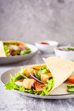 Tortilla wrap with cucumber, chicken and tomato on a plate. Mexican cuisine. Vertical view