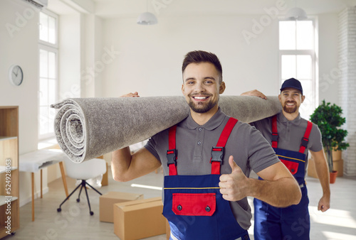 Portrait of smiling male movers carry carpet recommend good quality delivery or transportation service. Happy deliverymen or carriers help customer with moving or relocation. Shipping. photo