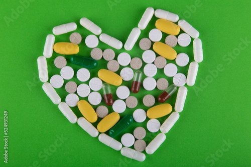 White, yellow, brown pills lay in heart shape on green background. Top view, flat lay photo
